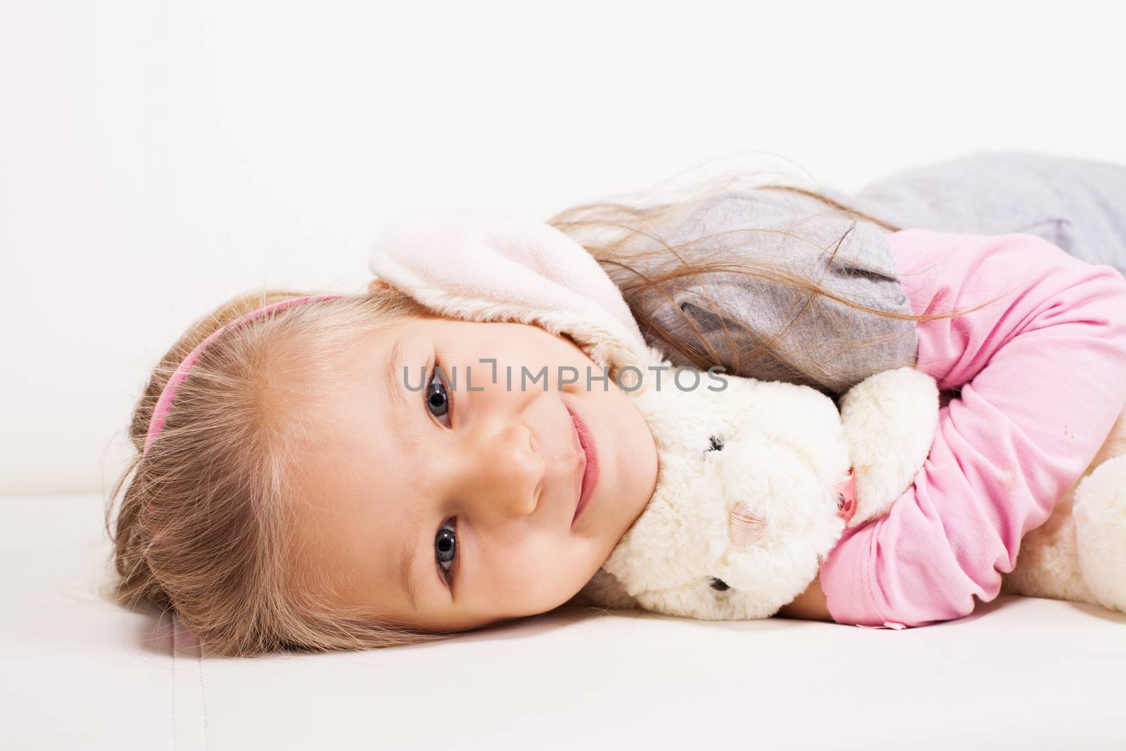 Cute little girl hugging soft toy on sofa at home.