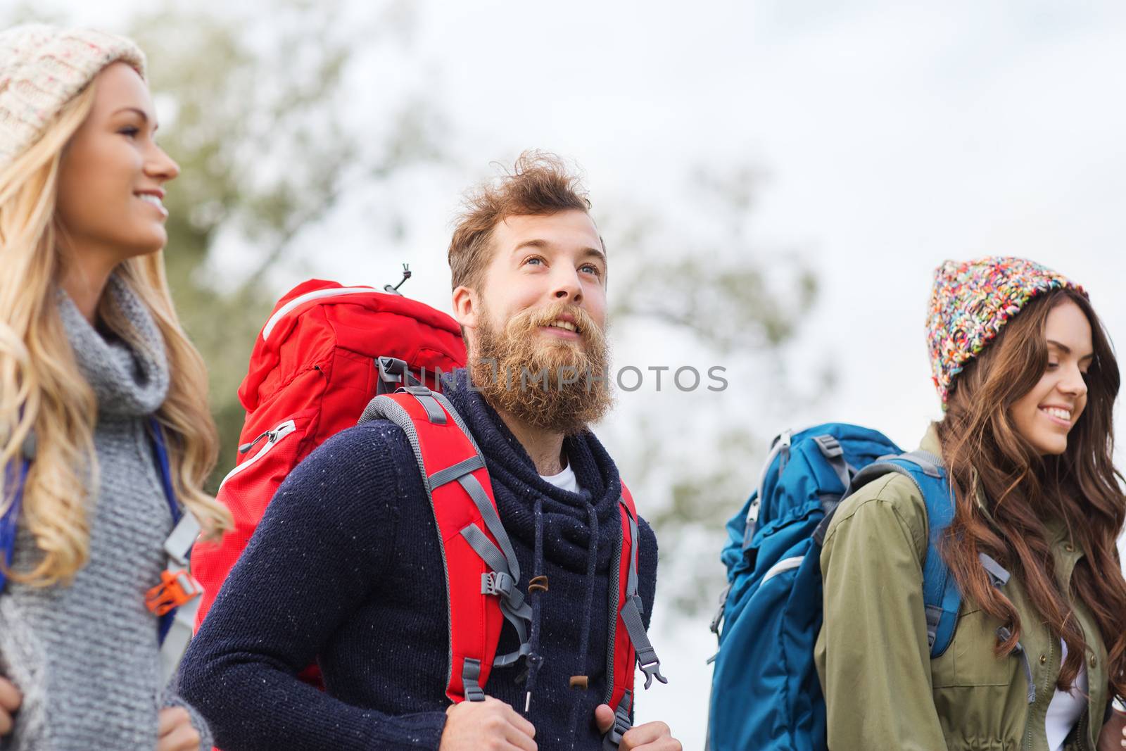 adventure, travel, tourism, hike and people concept - group of smiling friends walking with backpacks