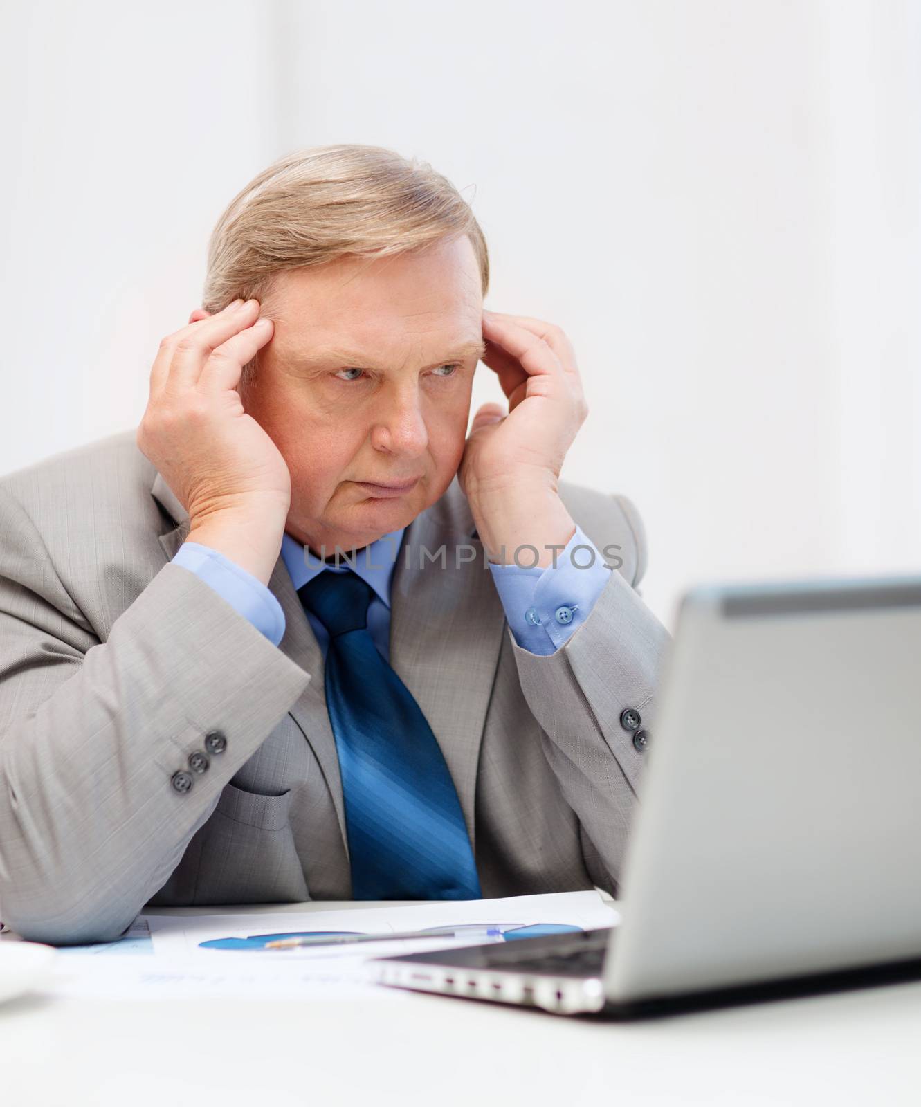 business, technology and office concept - upset older businessman with laptop and charts in office