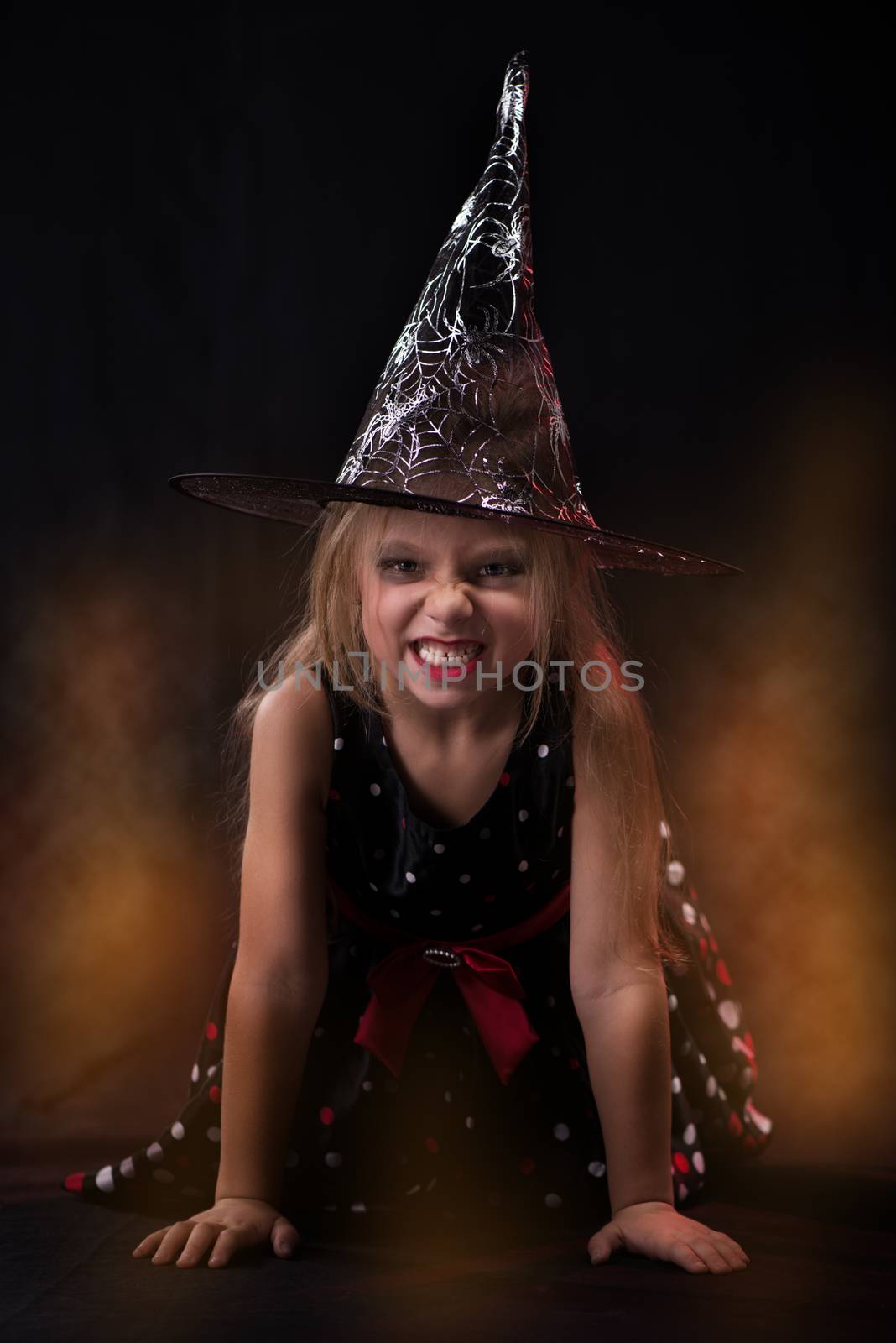 Little Halloween witch in dark clothing with evil face.
