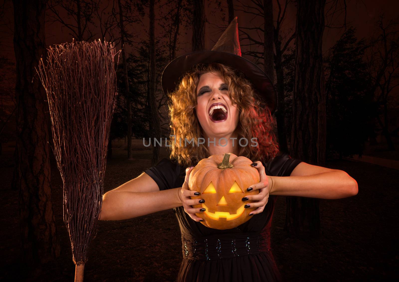 Young woman dressed like a witch. She is laughing and holding a pumpkin.