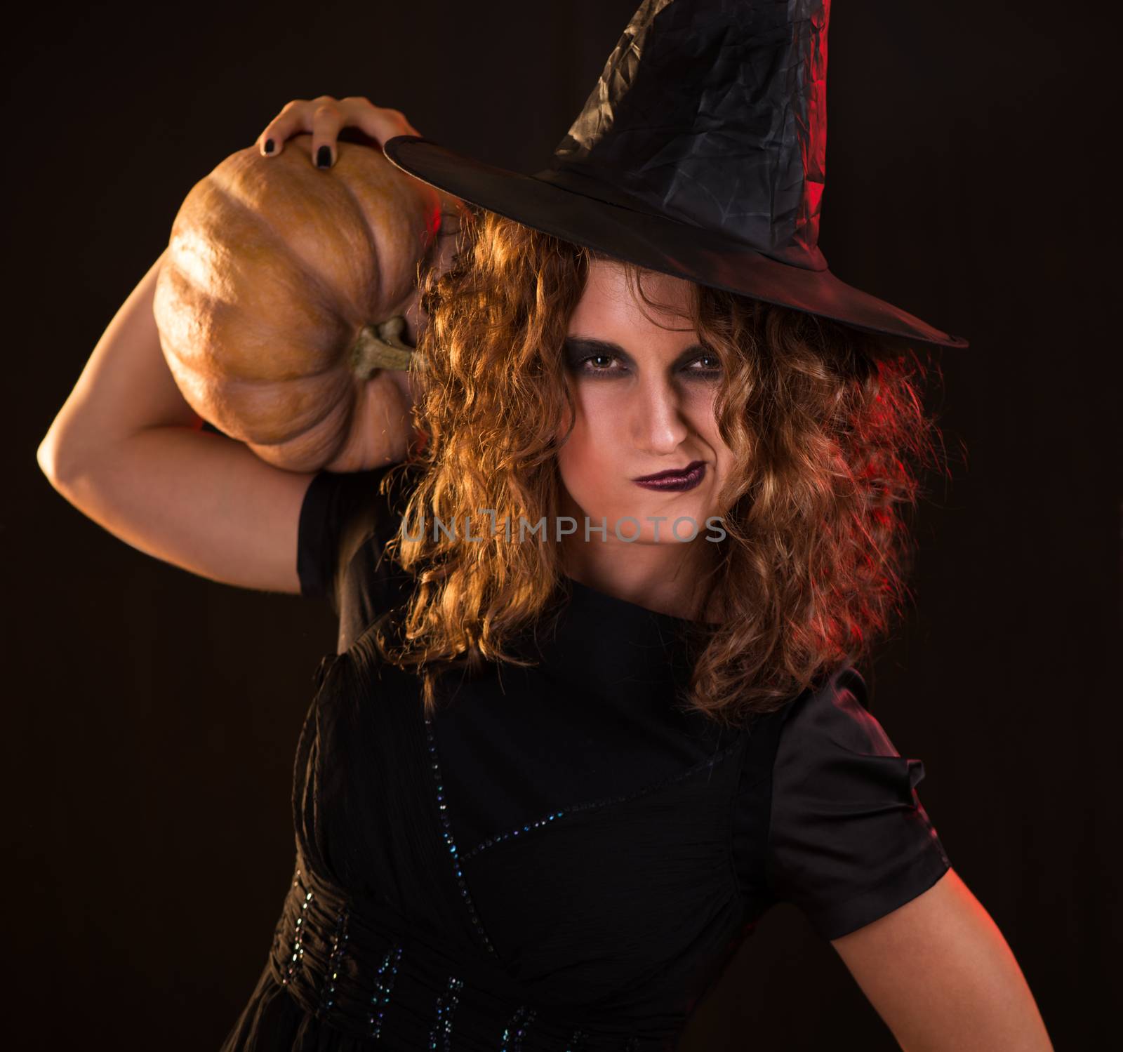 Young woman dressed like a witch. She is in dark clothing and holding a pumpkin.