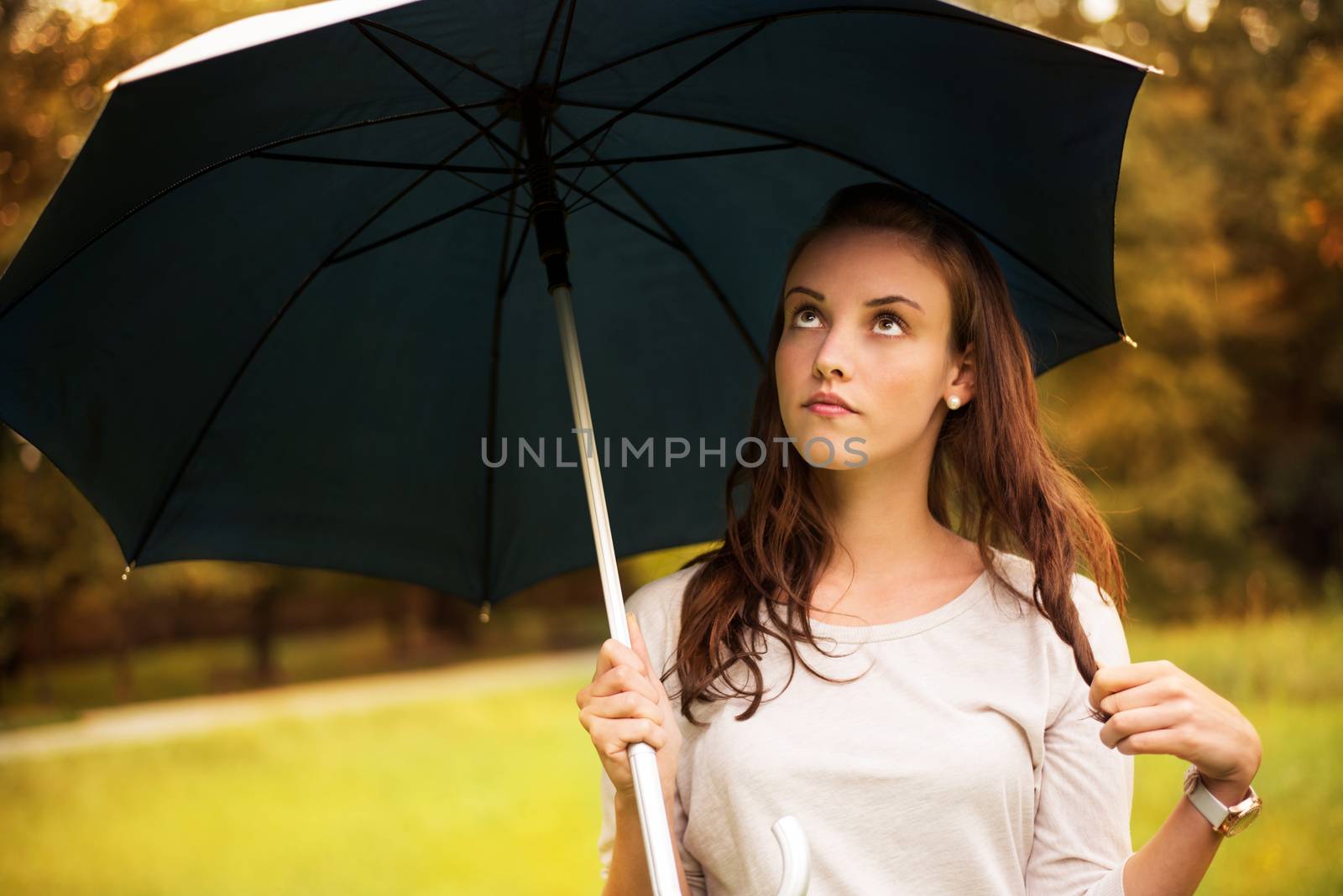 Portrait of young beautiful woman walking in rainy autumn park with umbrella.