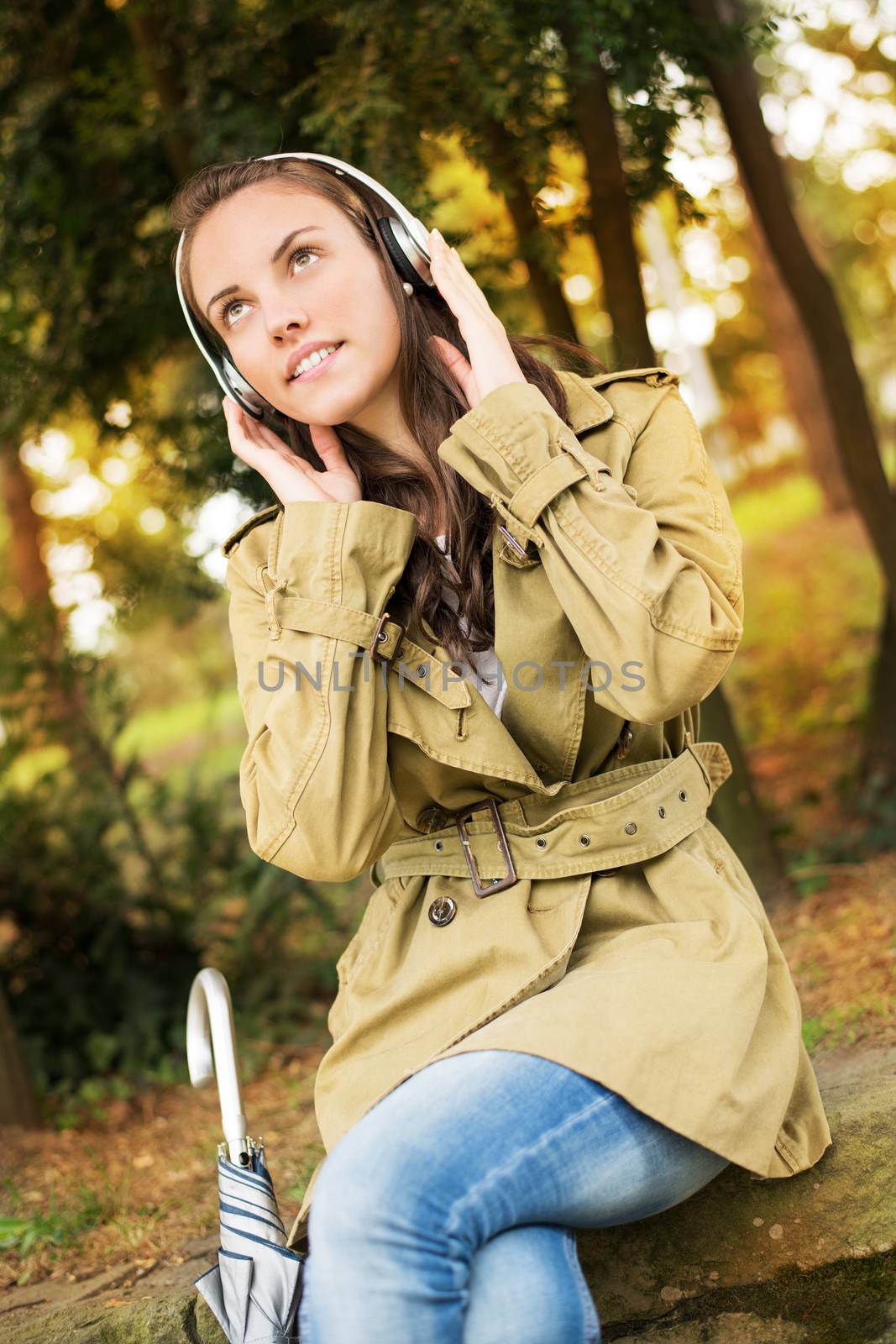 Young beautiful woman sitting in the autumnal park and listening to music.