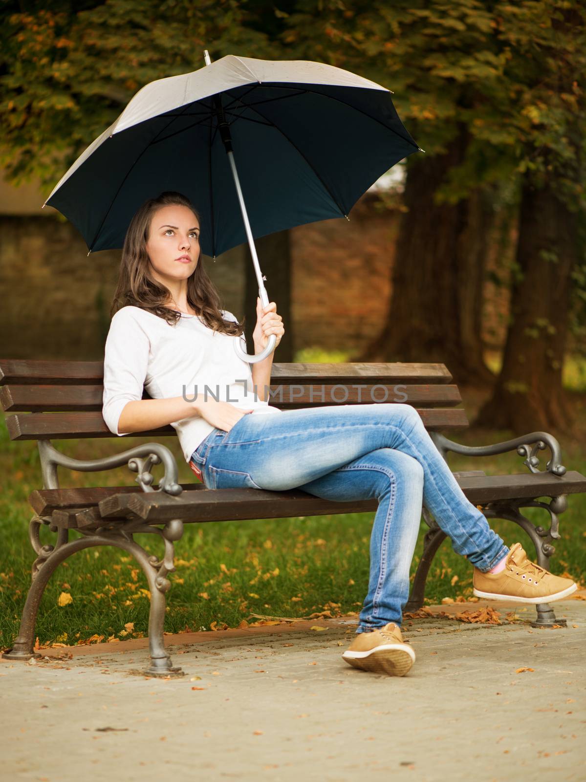 Lonely woman with umbrella sitting on the bench in the park.