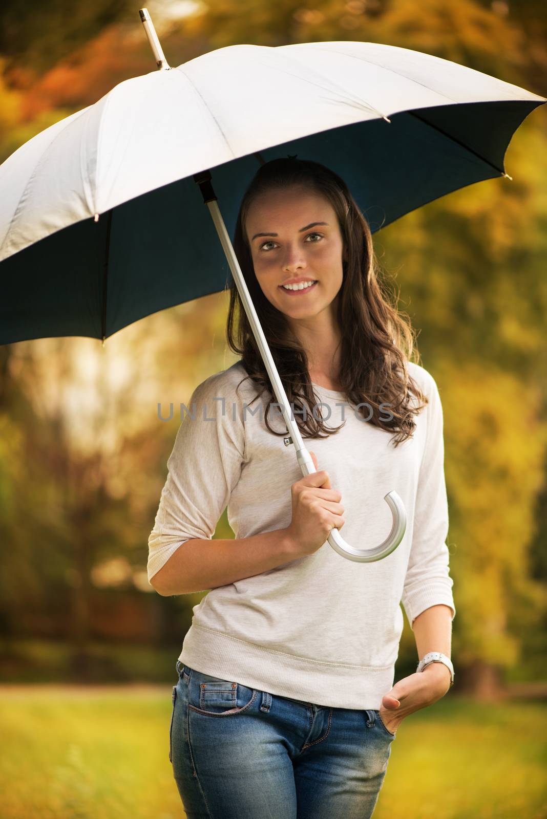 Young beautiful woman standing in rainy autumn park with umbrella.
