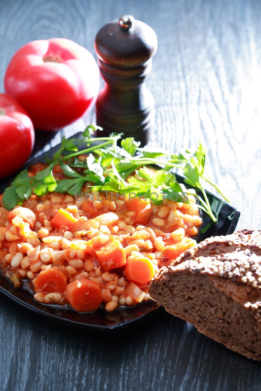 Black plate full of stewed beans on wooden background