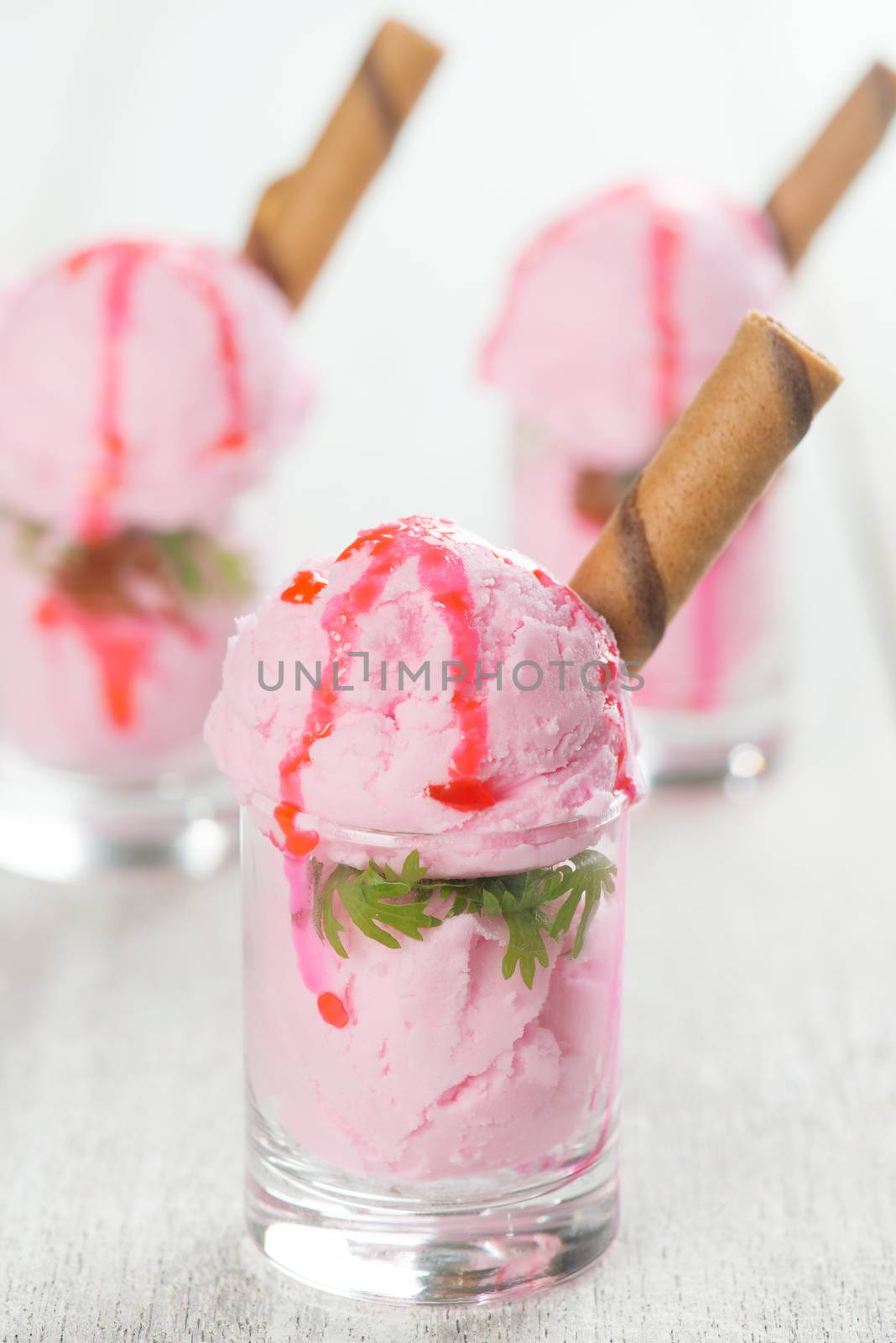 Scoops strawberry ice cream in glass cup with waffle on wooden vintage table background.