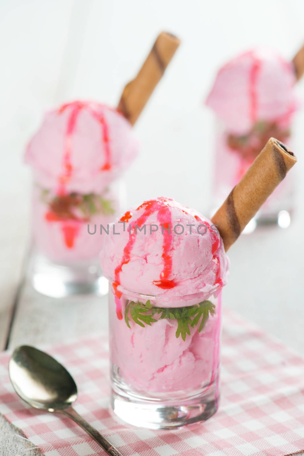 Scoops pink ice cream in glass cup with waffle on wooden vintage table background.