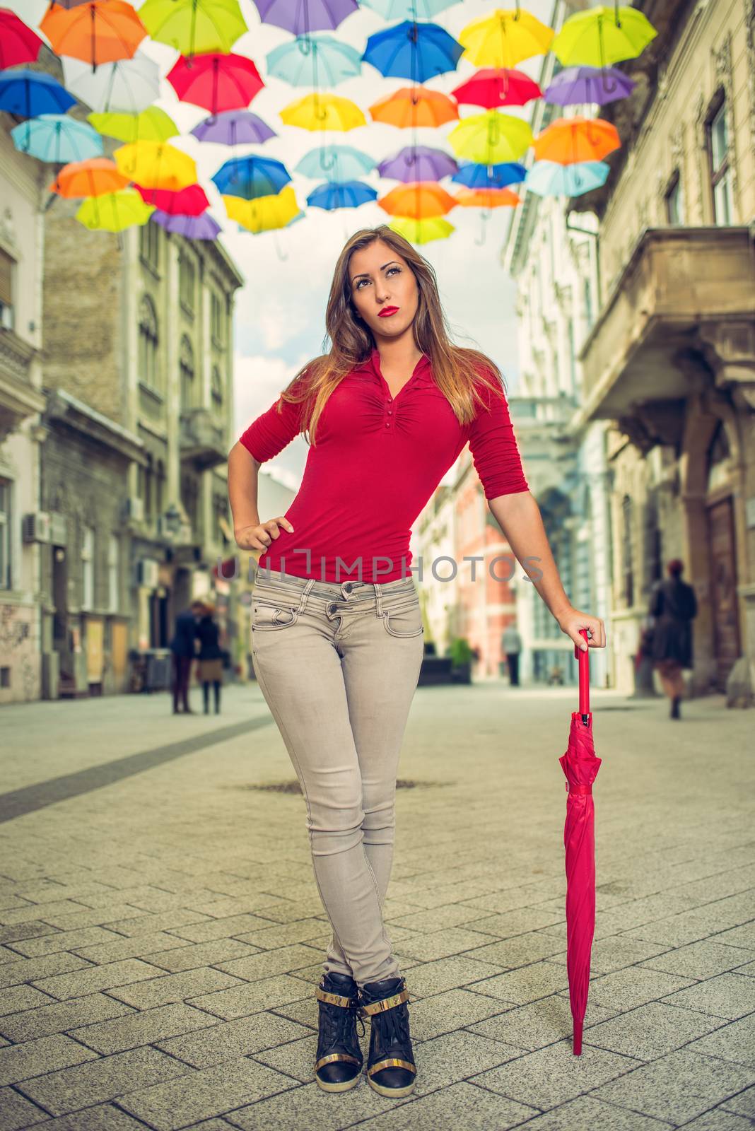 Beautiful young woman with red umbrella in the street decorated with lots of multicolor umbrellas.