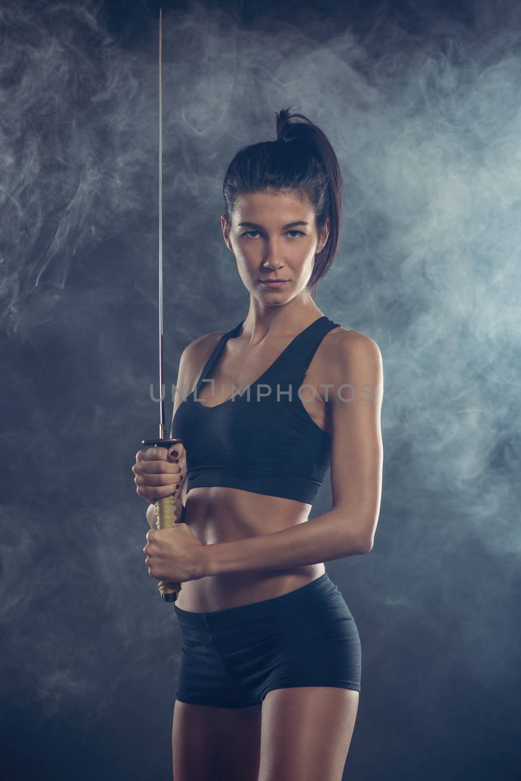 Portrait of a  beautiful young woman with sword and with a serious expression on her face looking at the camera. Dark background.
