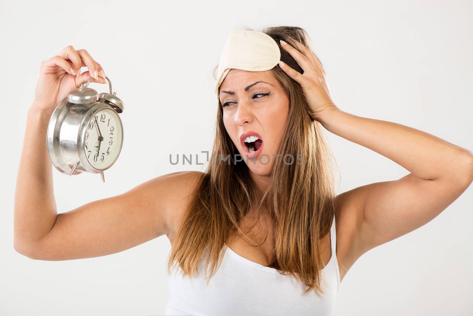 Beautiful young woman holding alarm clock. She is tired and lazy in morning.
