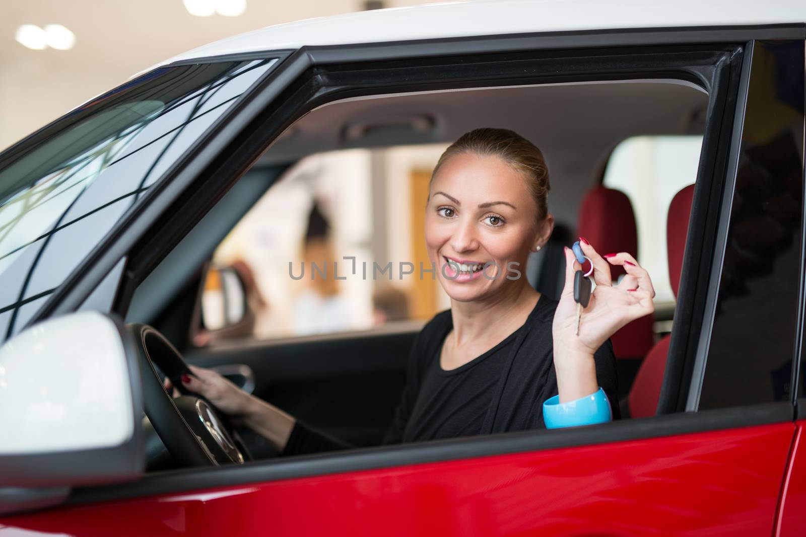 Young beautiful happy woman showing the keys of new car through car window. Looking at camera.