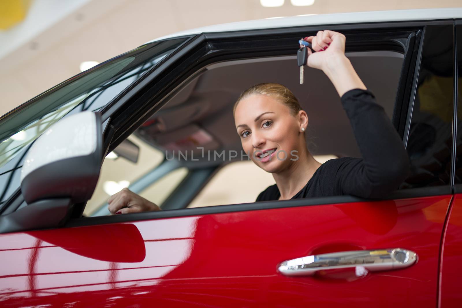 Young beautiful happy woman showing the keys of new car through car window. Looking at camera.