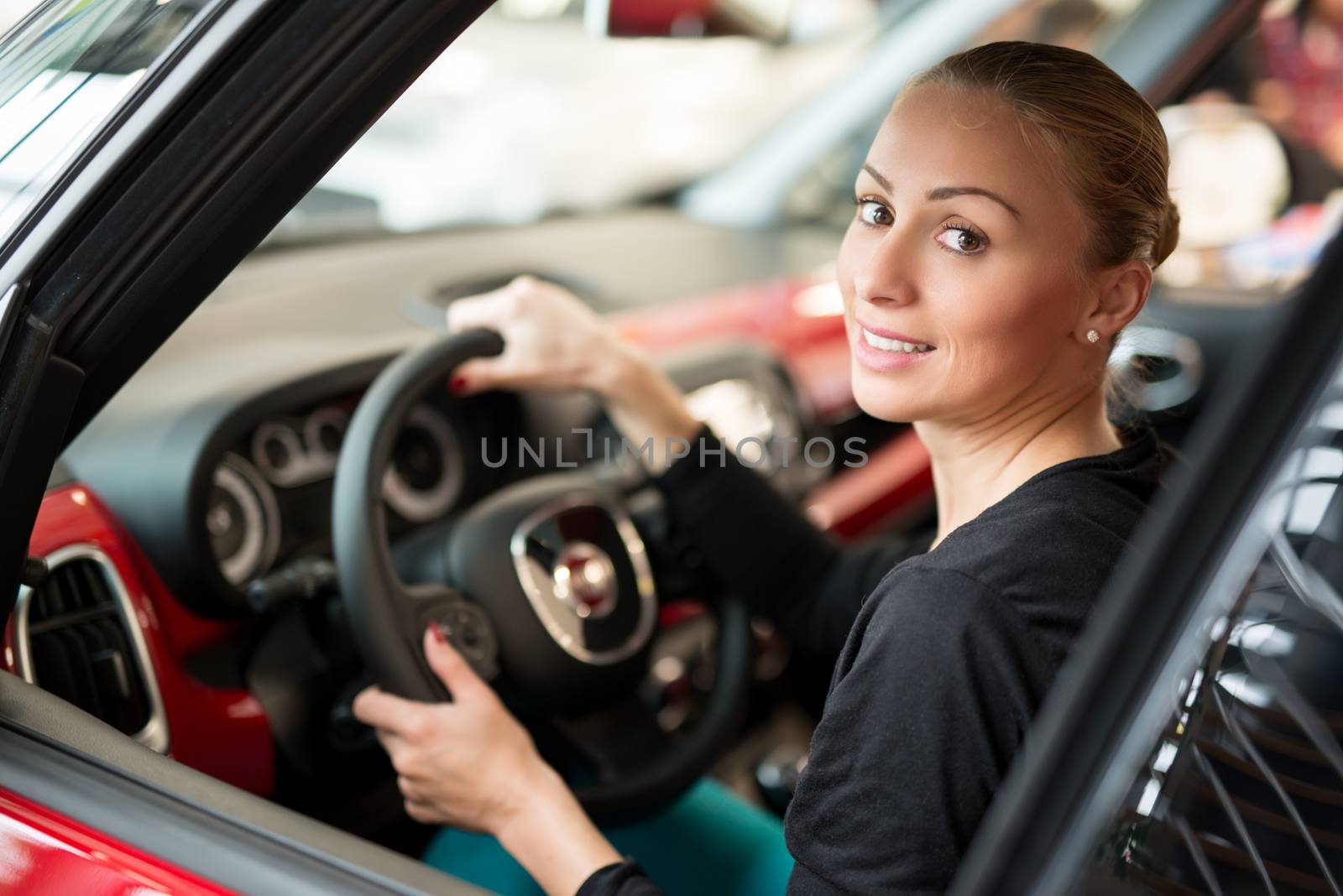 Young beautiful happy woman sitting at the wheel new car and looking through car window. 