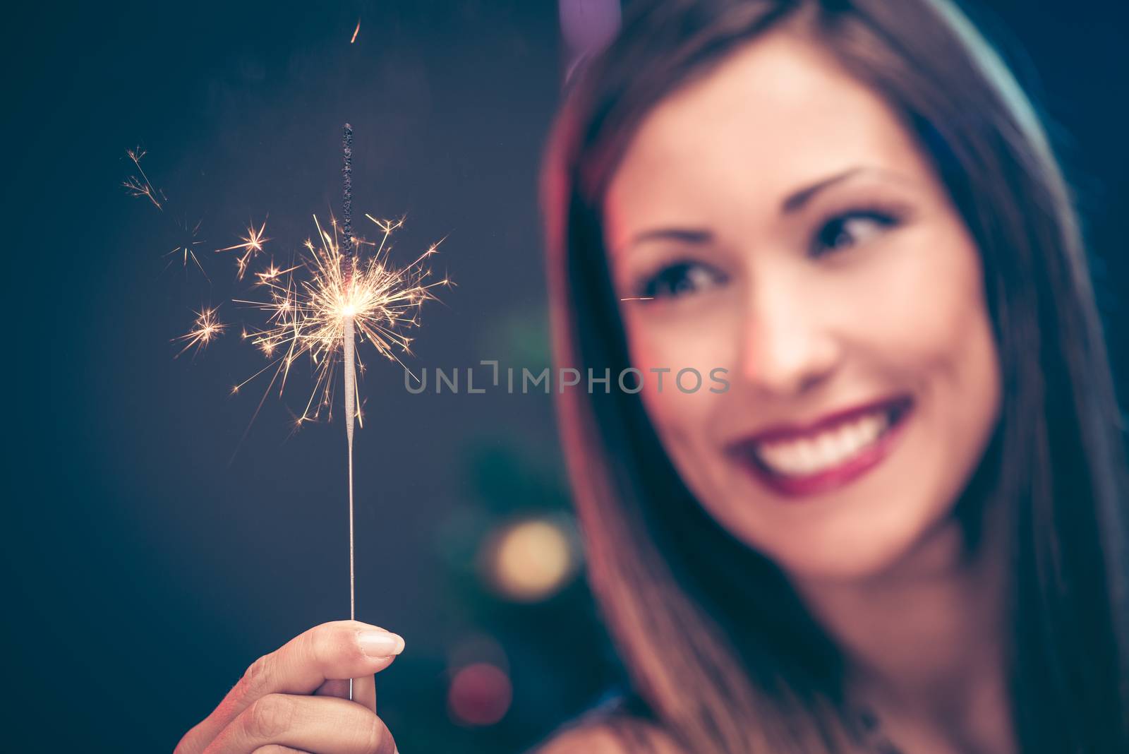 Close-up of a beautiful woman holding with sparkler. Focus on foreground, on sparkler.