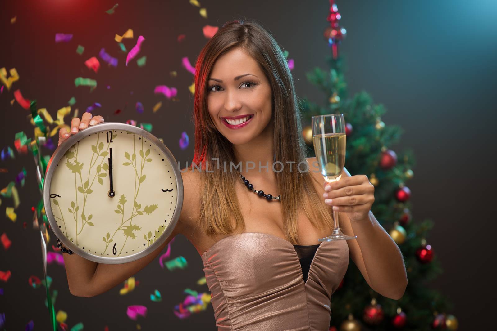 Happiness beautiful woman celebrating New Year. She is showing midnight on the clock and toasting with champagne. Confetti is the air.