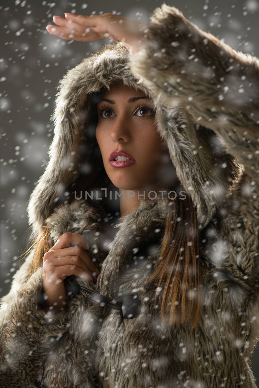 Portrait of a beautiful young woman in winter clothes worried peeking through snow far away.