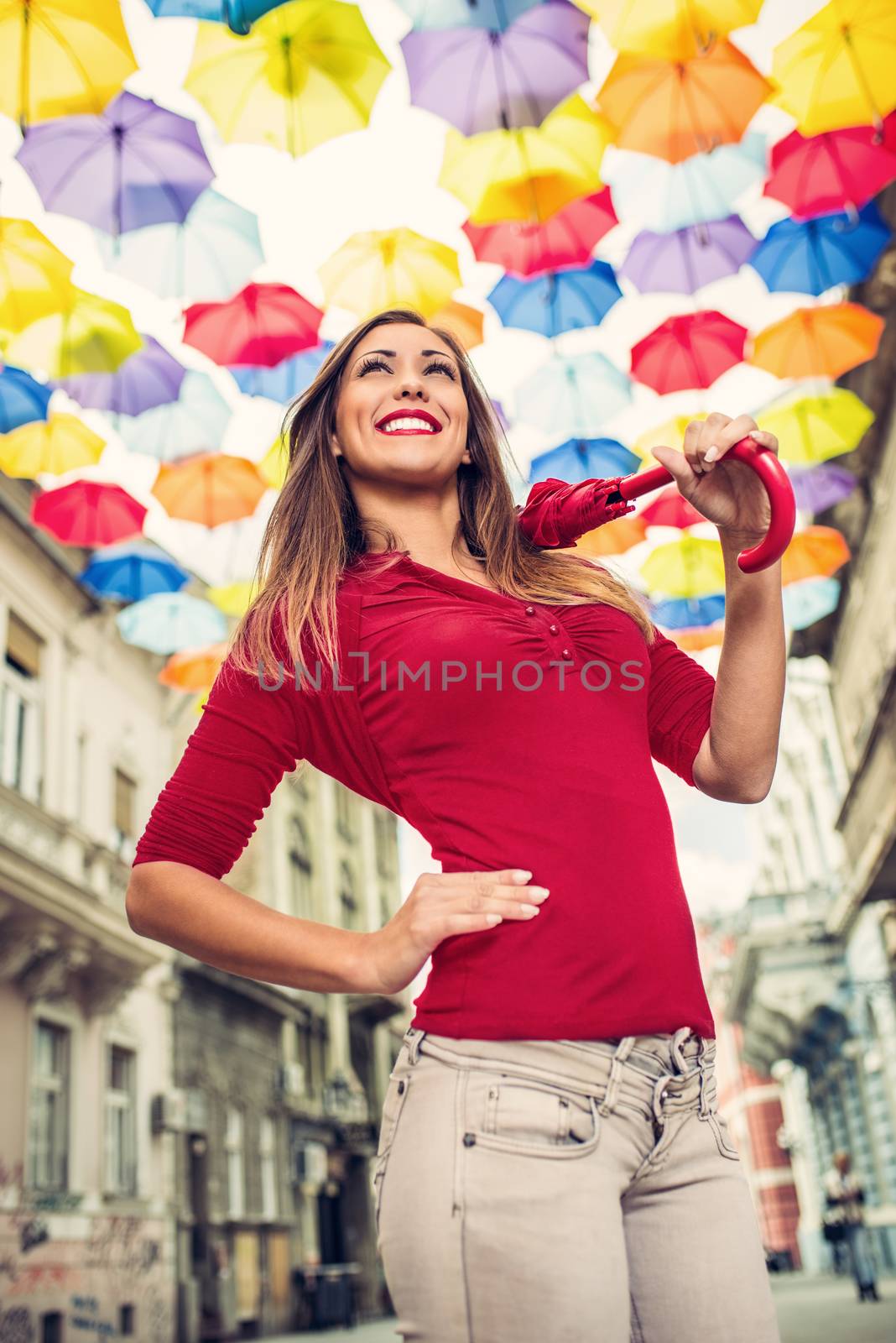 Beautiful young woman with red umbrella walking down the street decorated with lots of multicolor umbrellas.