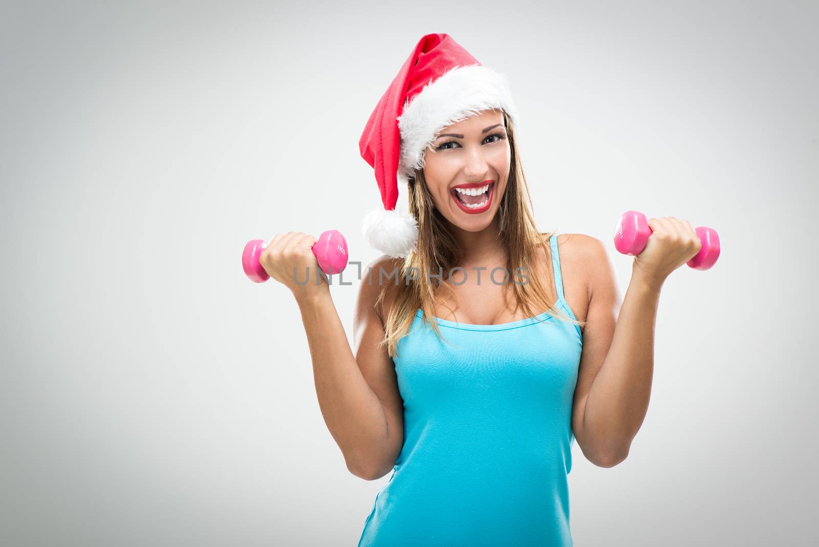 Beautiful fitness woman wearing santa hat doing exercise training arms lifting dumbbells.