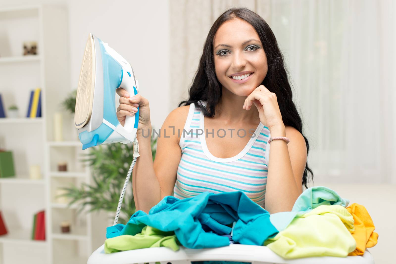 Young beautiful woman with basket laundry for ironing. Looking at camera and holding iron.