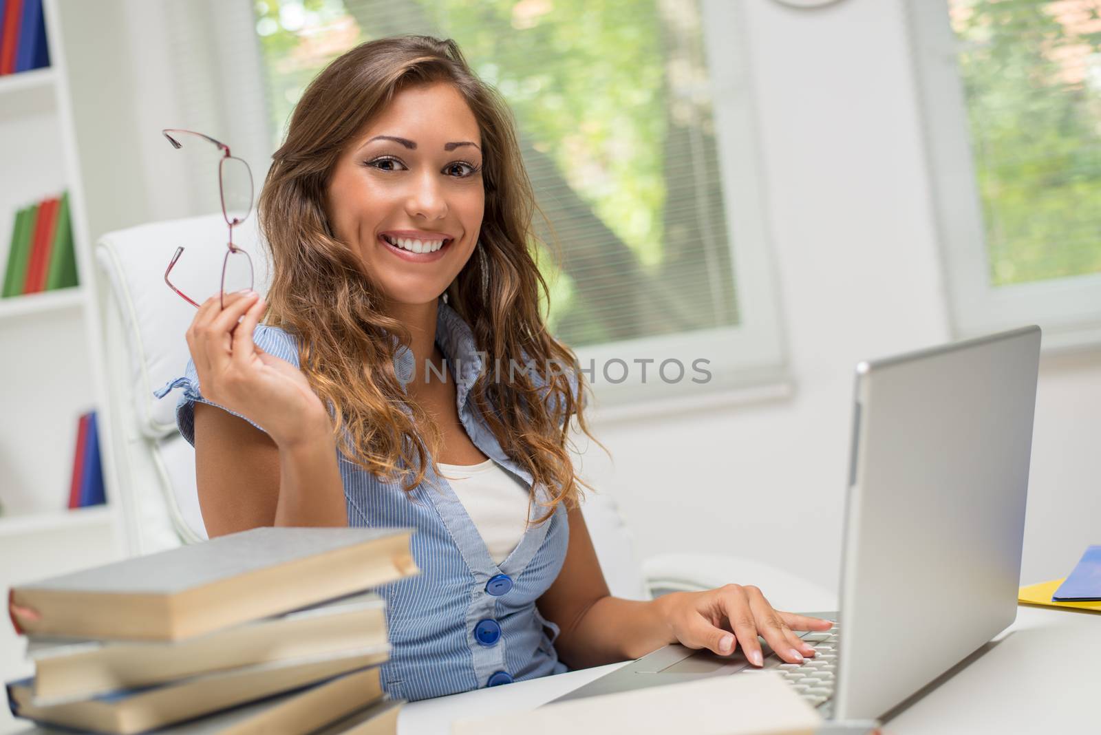 Beautiful teenage girl with many books and laptop learning in the library.