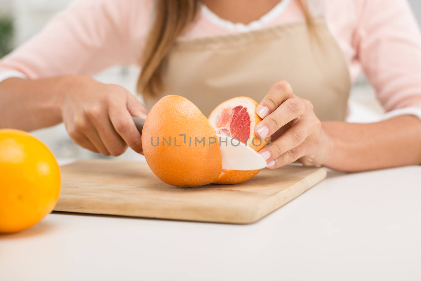 Close-up of a female hands cutting red grapefruit on the kitchen board.