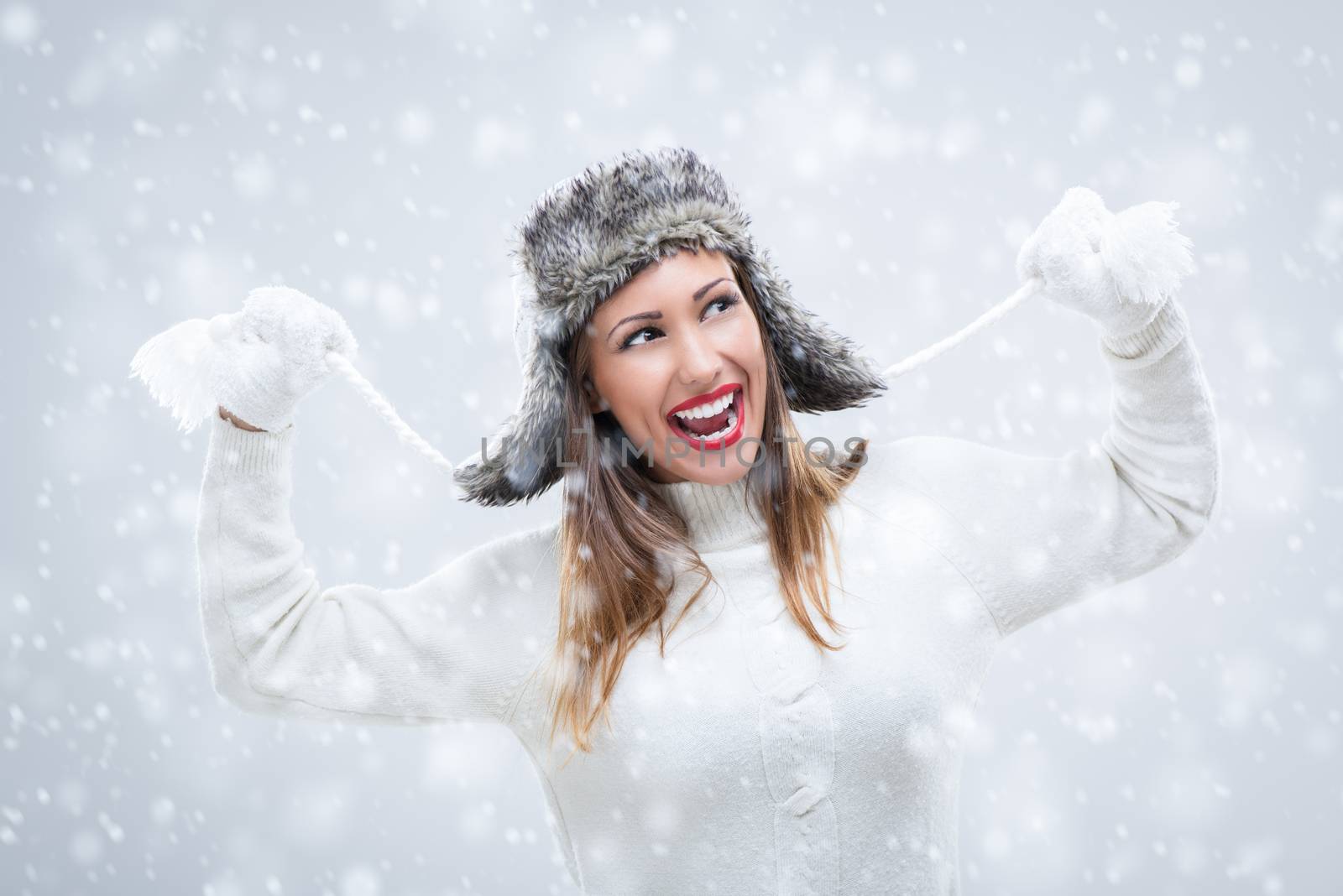 Cheerful beautiful young woman in warm clothing having fun while snowing.