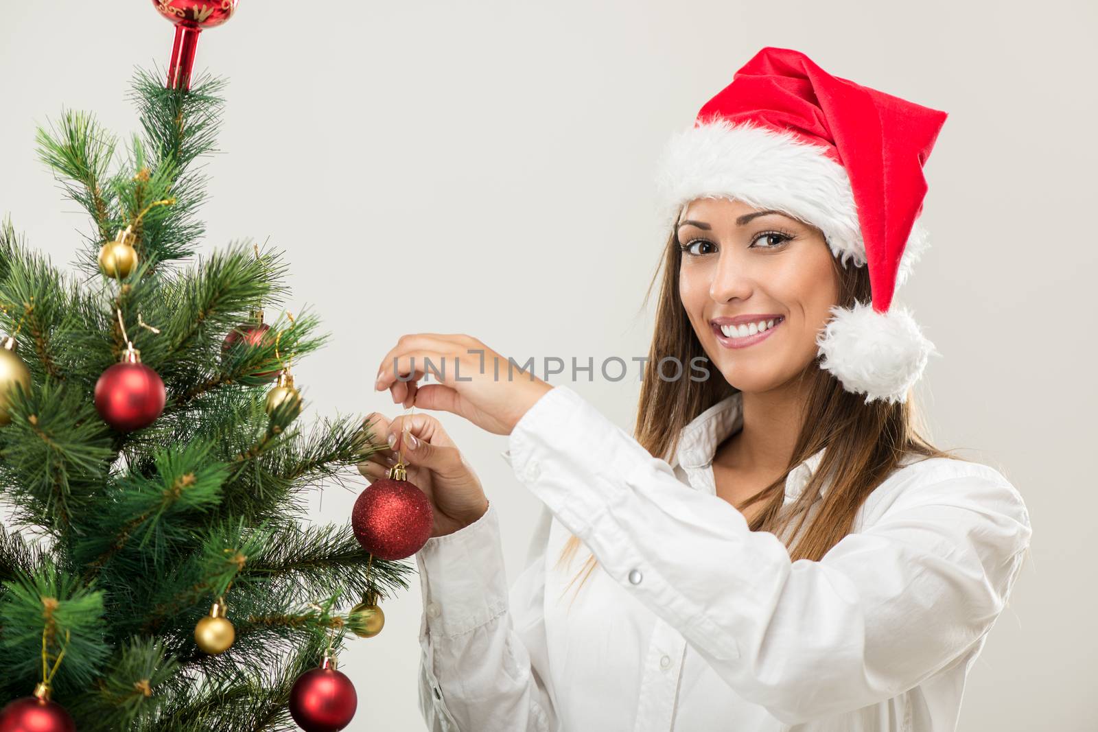 Portrait of a beautiful young businesswoman wearing santa hat and decorating Christmas tree.