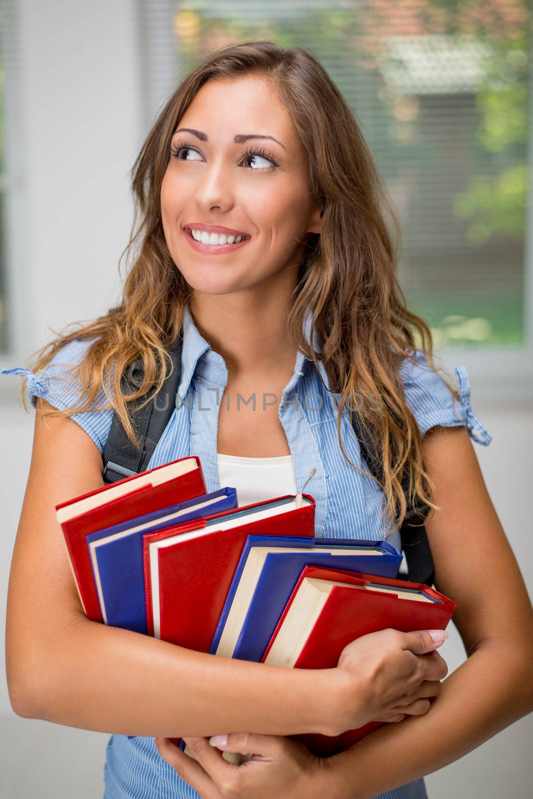 Happy beautiful teenage girl with Colorful books and school bag.