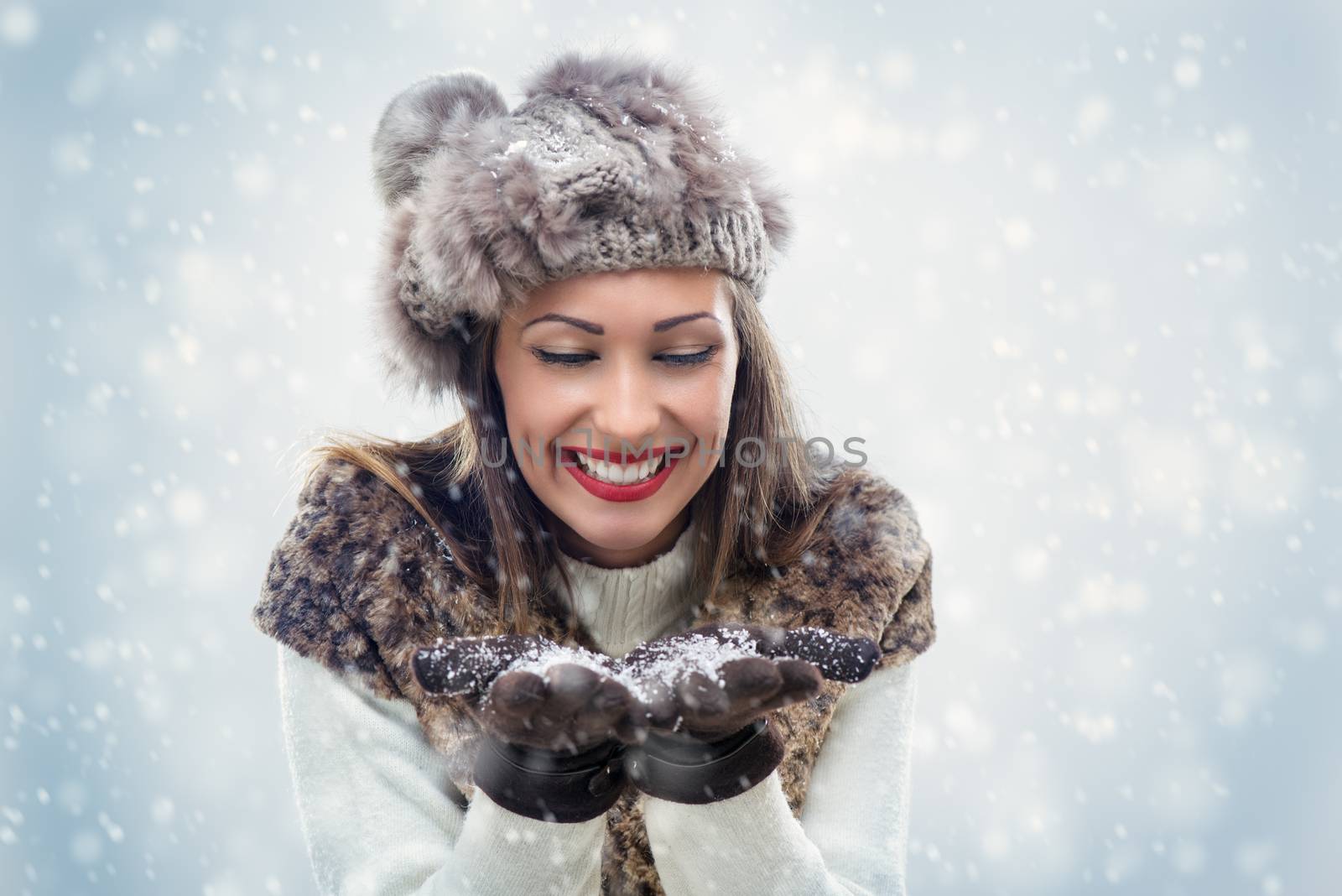 Beautiful young woman in winter clothes blowing snowflakes, which holds in her hands.