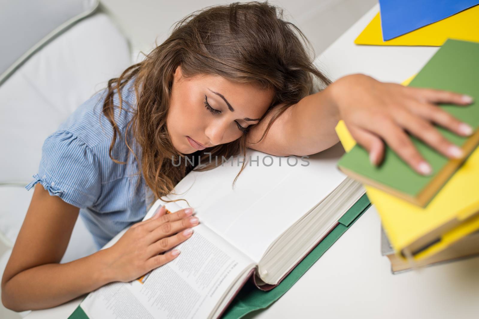 Portrait of beautiful tired teenage girl sleeping on the books in the library.