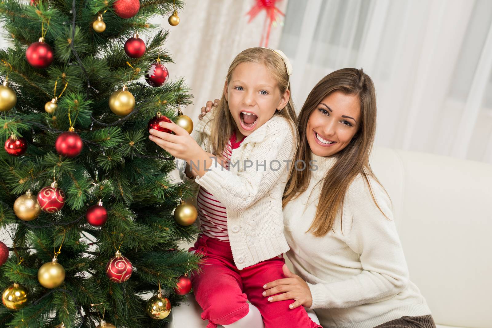 Young mother and her daughter decorating Christmas tree at home. 