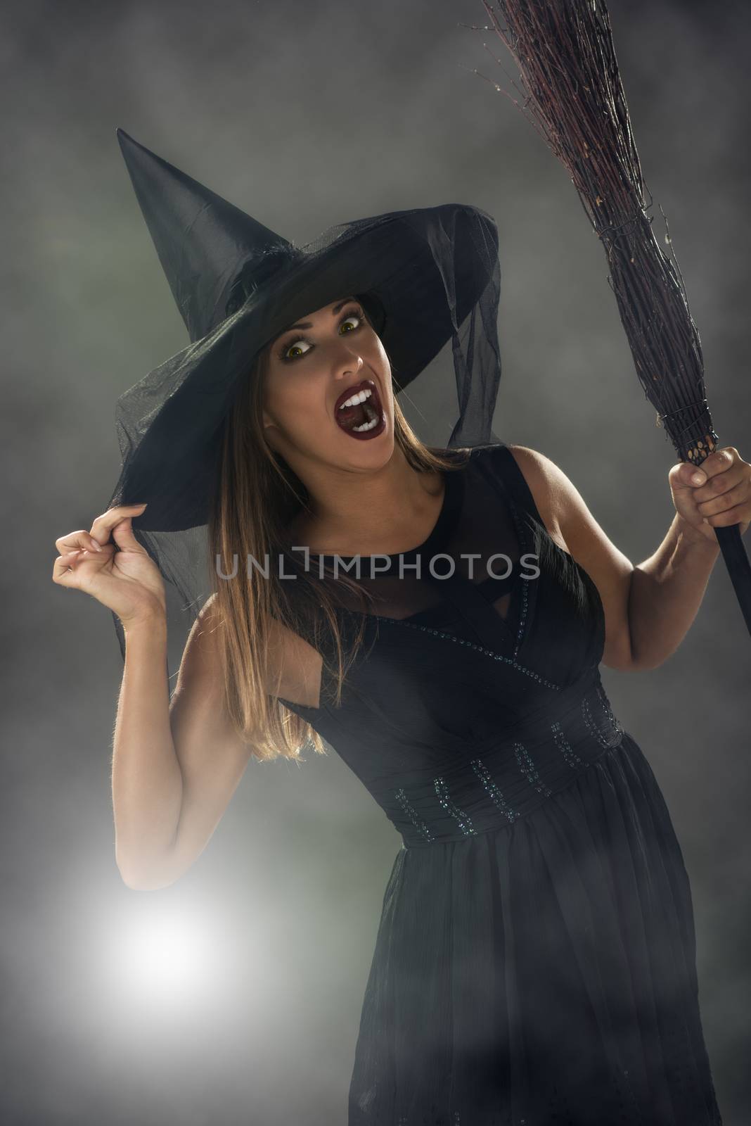 Young woman dressed like a witch. She is in dark clothing and holding a broom.