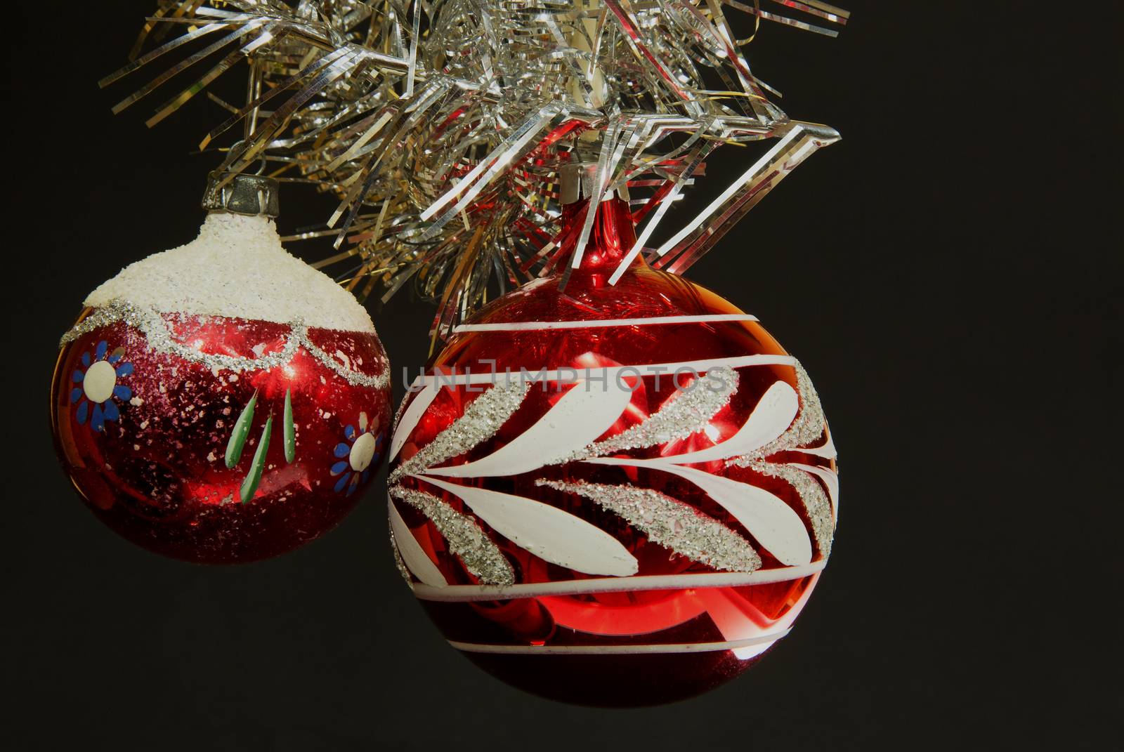 Two red Christmas balls with ornaments of imposed from the top of an ornate silver chain. The whole on a black isolated background