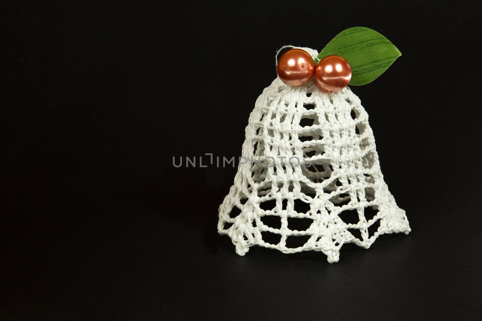 White bell, Christmas Tree ornament hand-made yarn with two red beads and a green leaf.isolated on a black background.Close,horizontal view.
