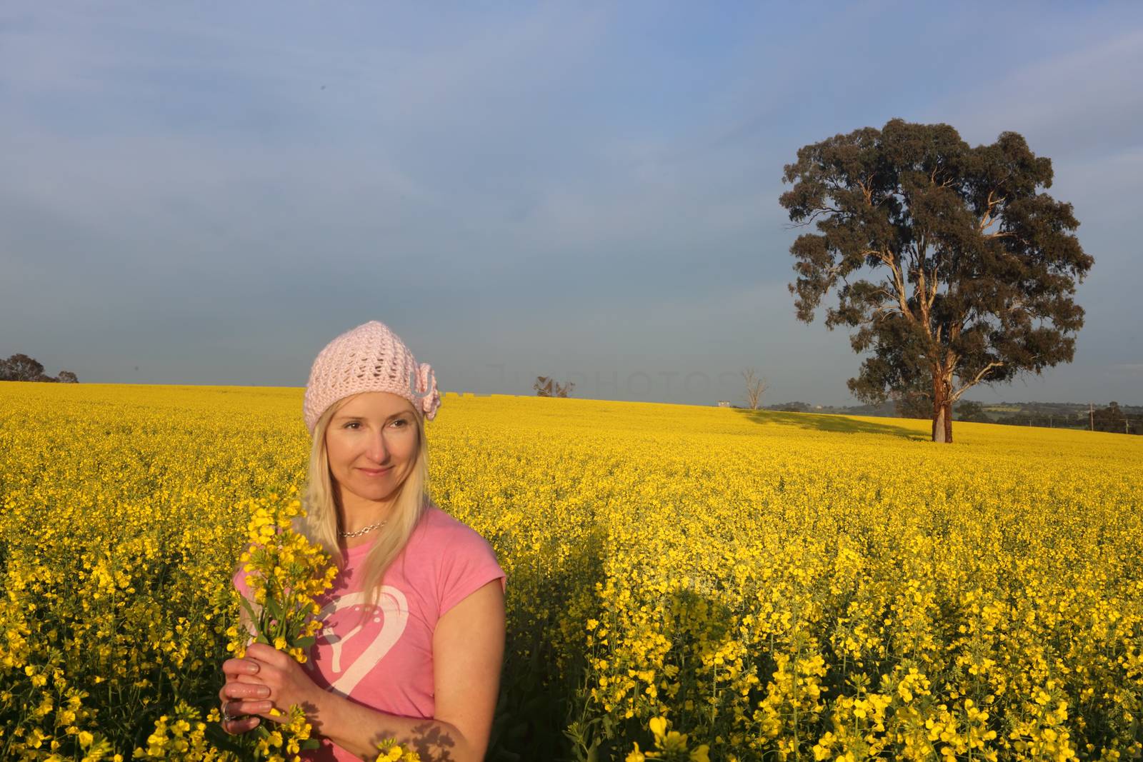 Smiling woman standing in a field of golden flowering canola rapeseed farmland in early morning sunlight