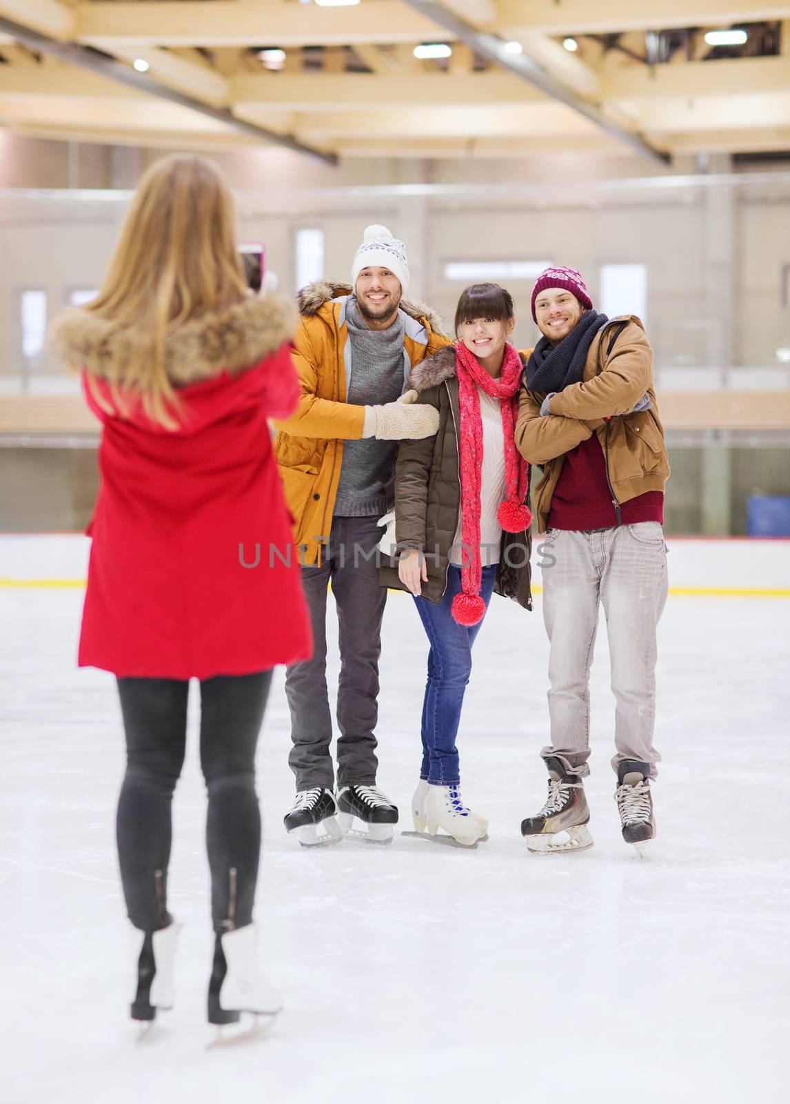 people, friendship, technology and leisure concept - happy friends taking photo with smartphone on skating rink