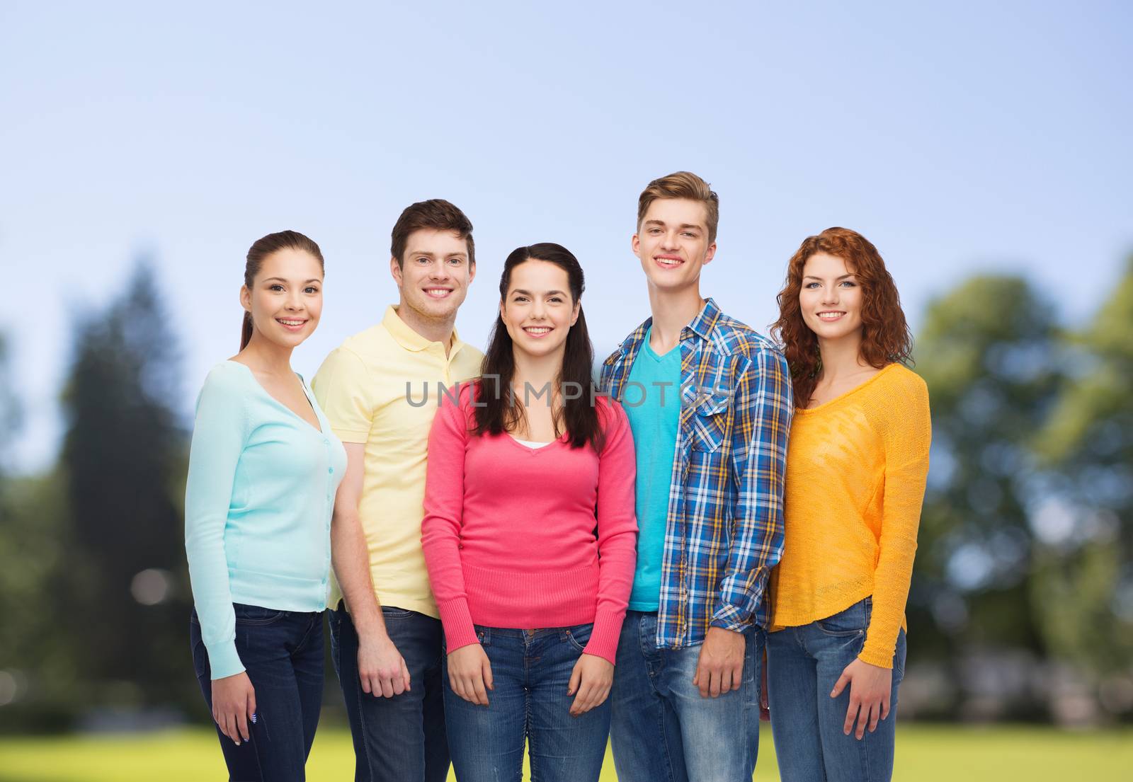 friendship, summer vacation, nature and people concept - group of smiling teenagers standing over green park background