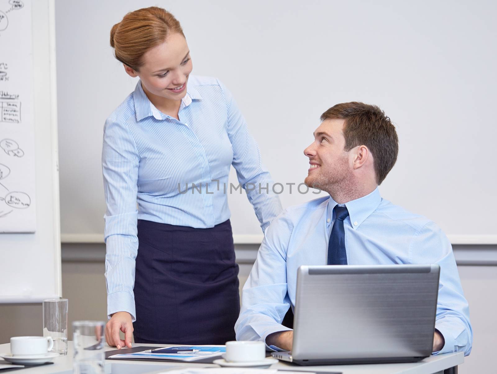 smiling businesspeople with laptop in office by dolgachov