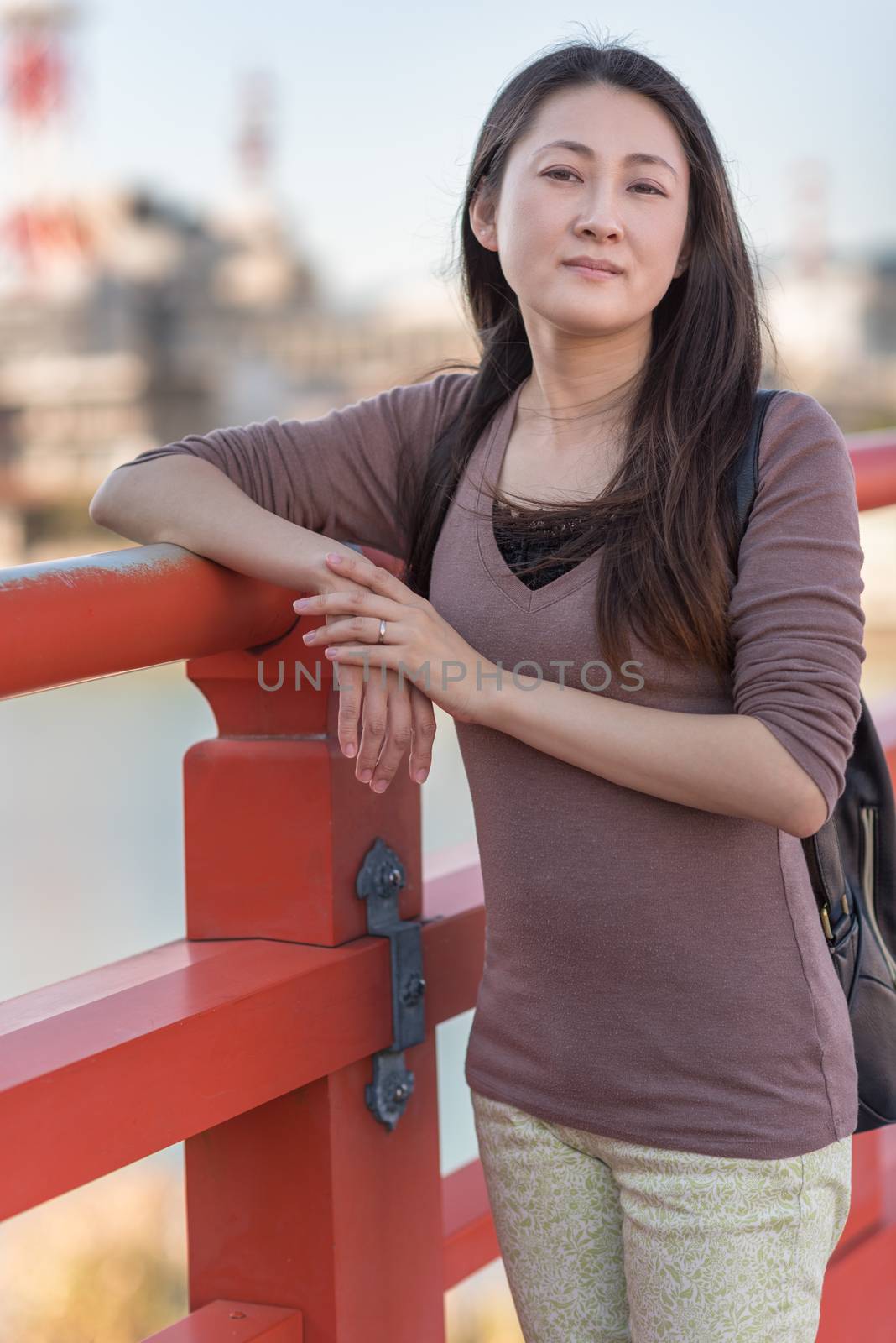 A young Japanese girl posing on an orange bridge in Japan.