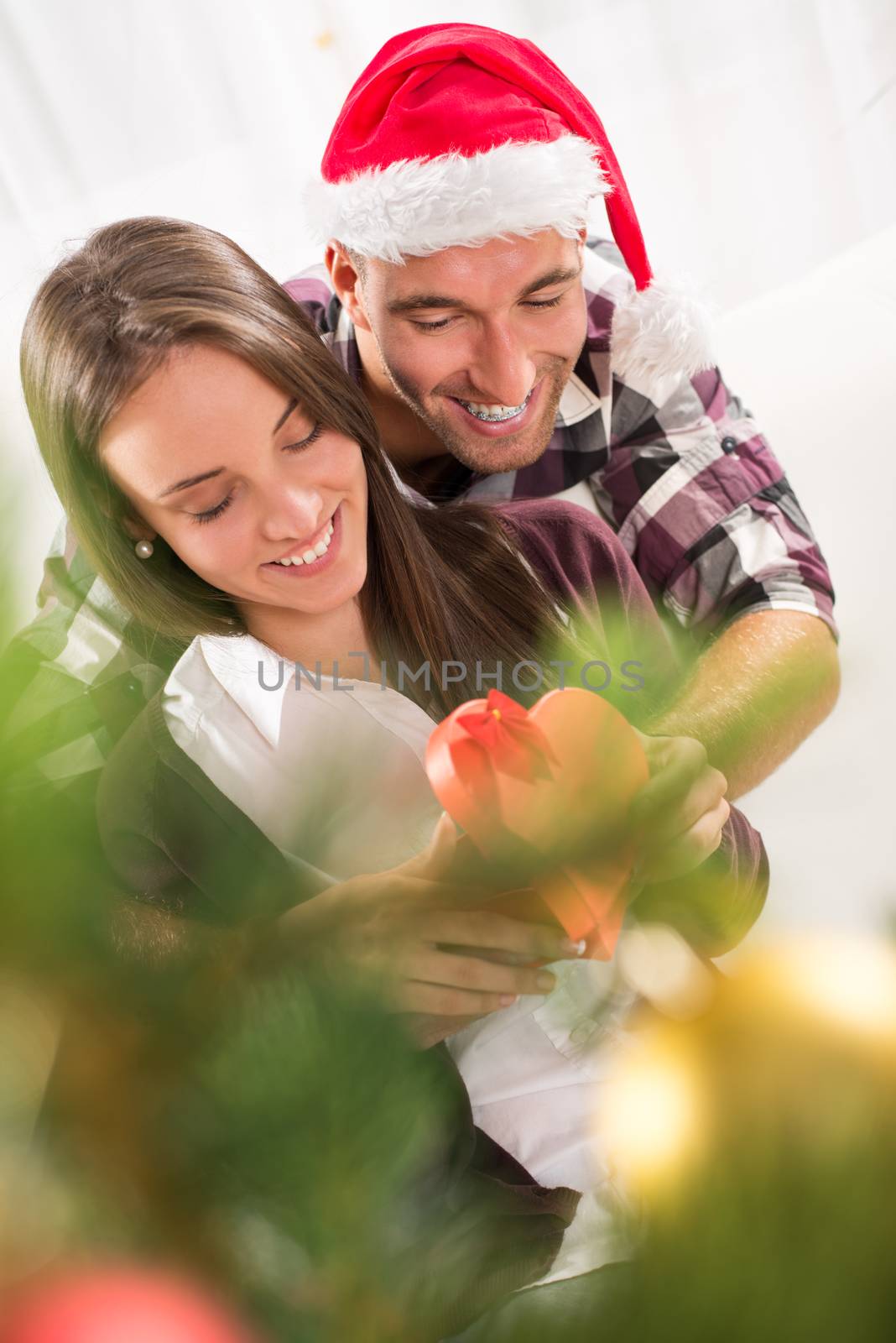 Young man gives his girlfriend a Christmas gift. She is happy while opening gift box.