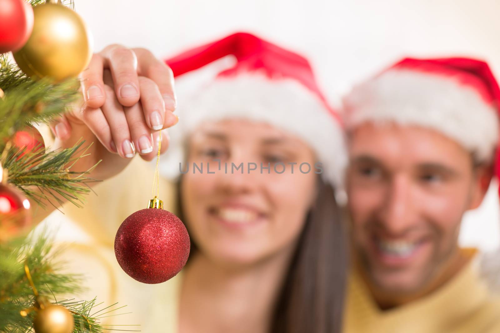 Happy young couple enjoy decorating Christmas tree at home. Selective Focus, focus on christmas ball.