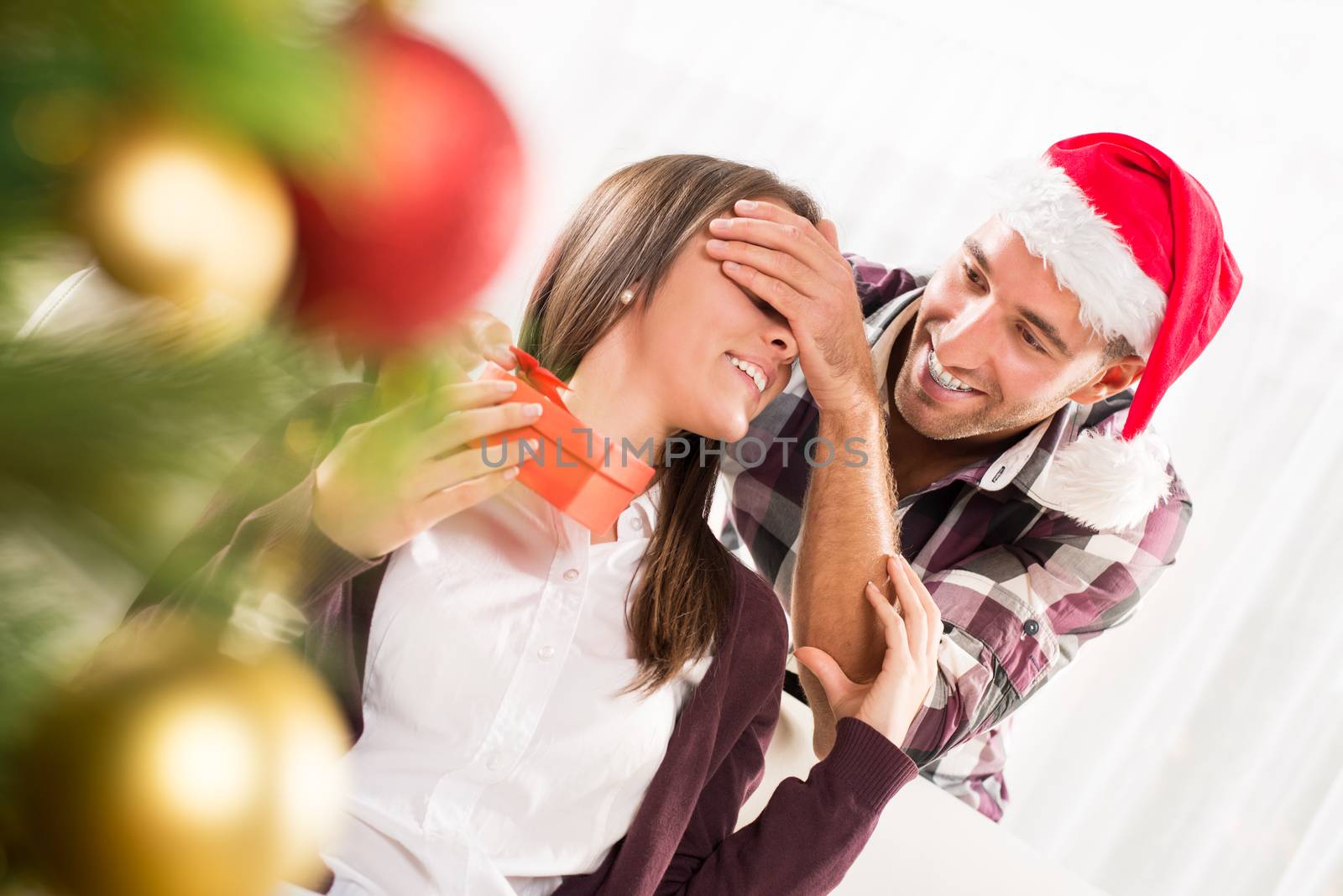 Young man gives his girlfriend a Christmas gift holding his hand over her eyes.