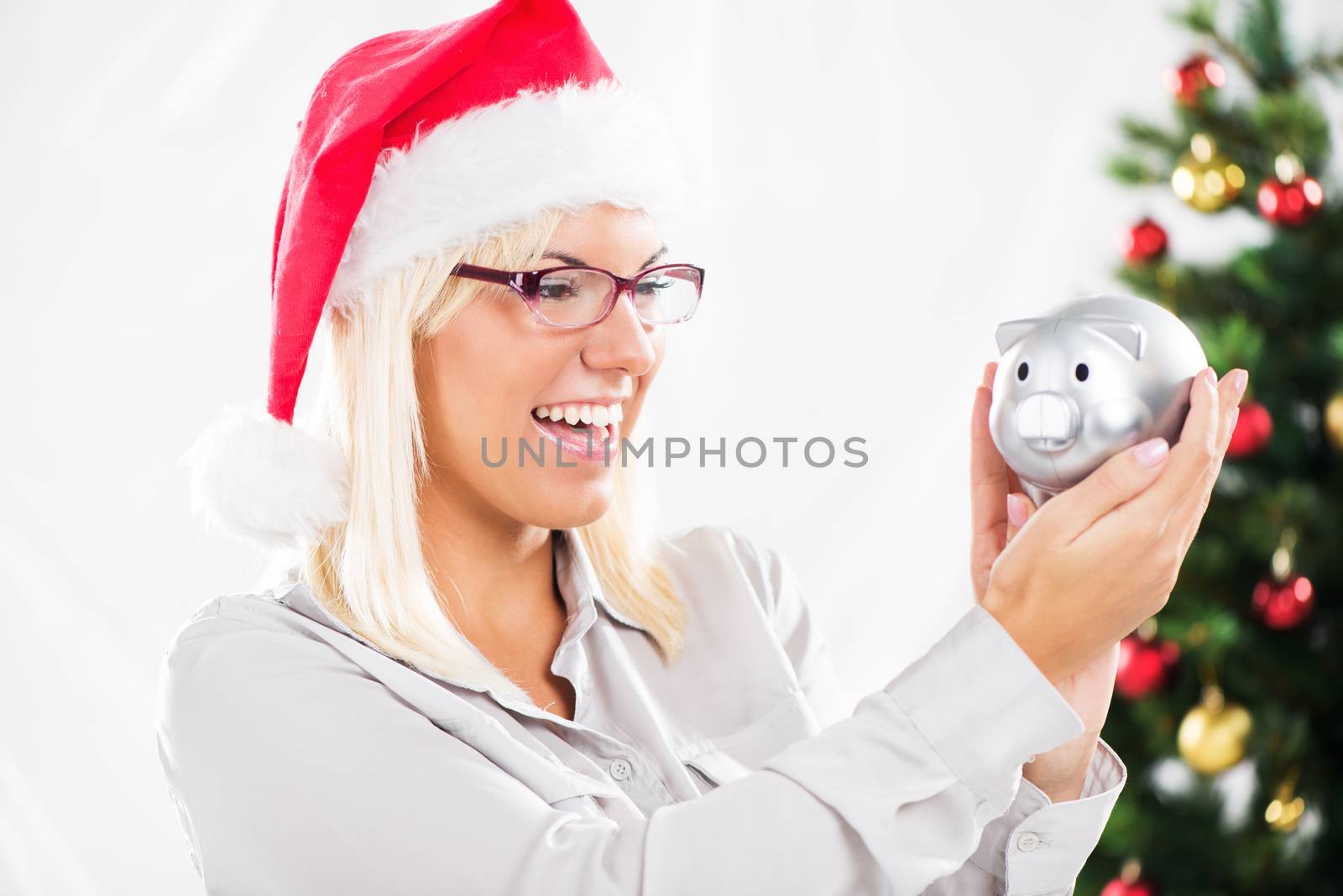 Young beautiful woman with glasses and Santa Hat holding Piggy Bank.