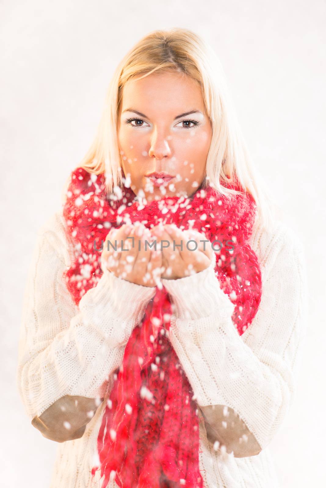 Beautiful happy winter girl blowing snow into the air.