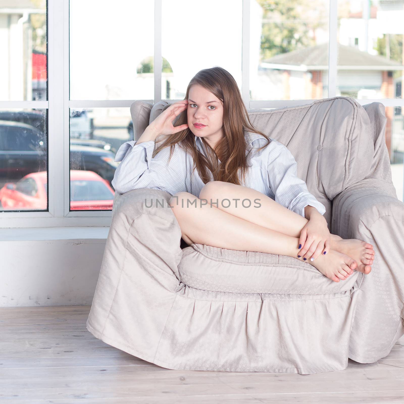 Young woman at home sitting on modern chair in front of window relaxing in her living room
