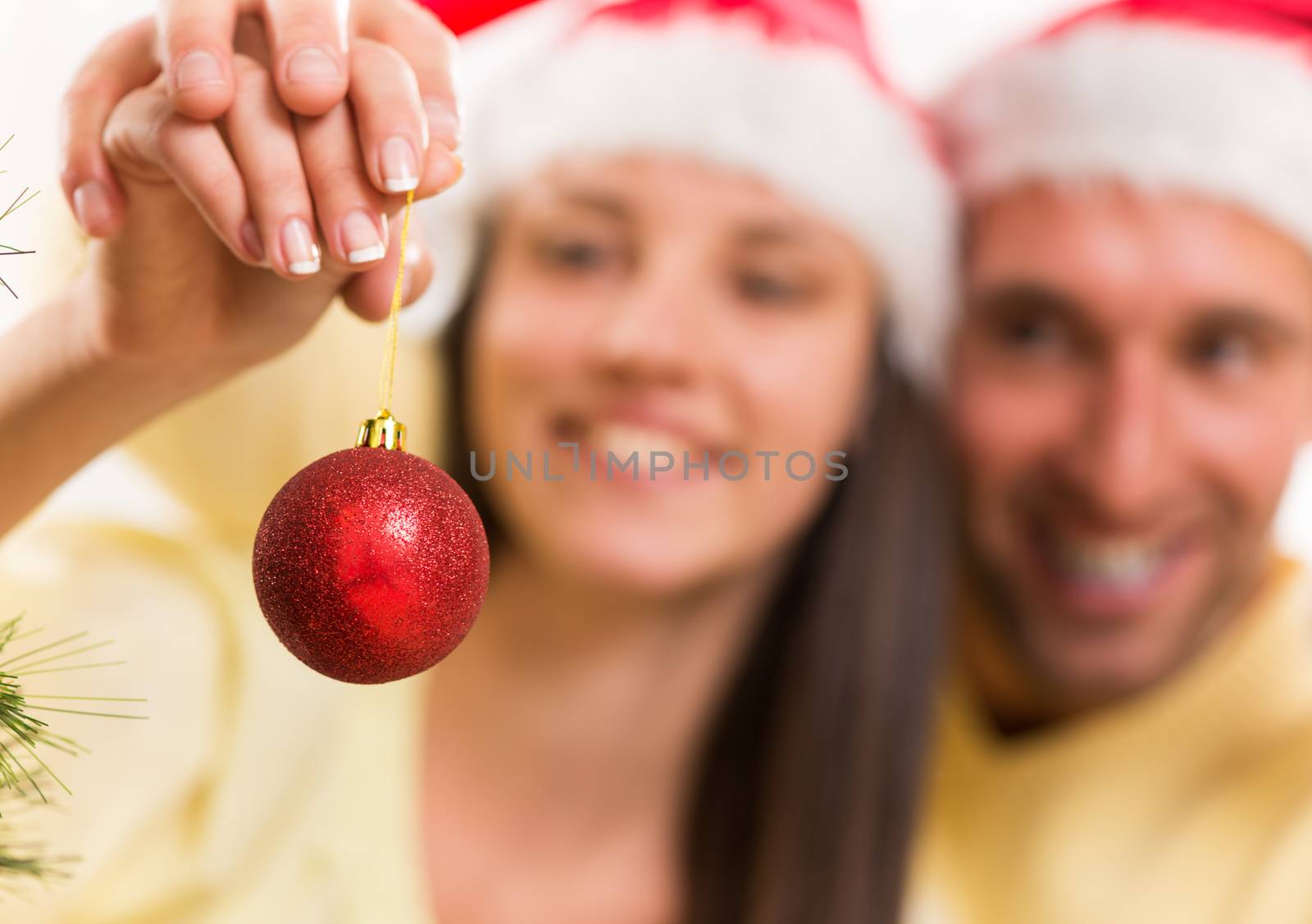 Happy young couple enjoy decorating Christmas tree at home. Selective Focus, focus on christmas ball.