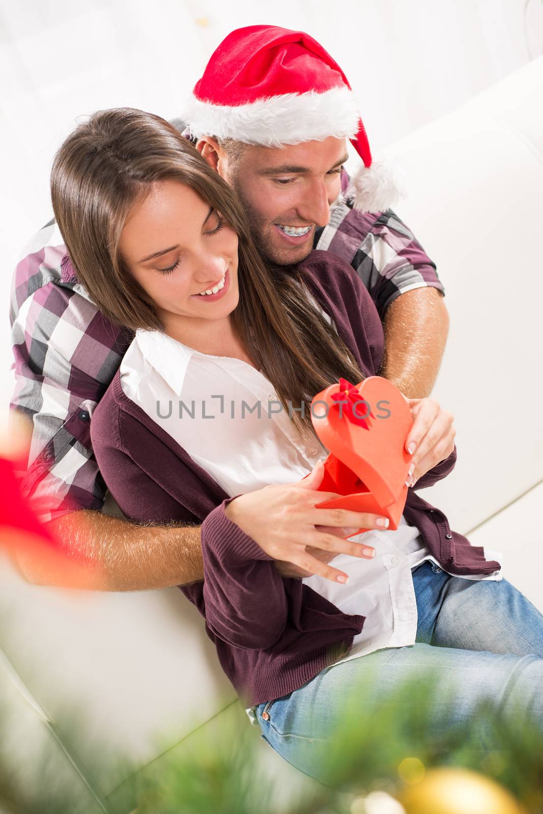 Young man gives his girlfriend a Christmas gift. She is happy while opening gift box.