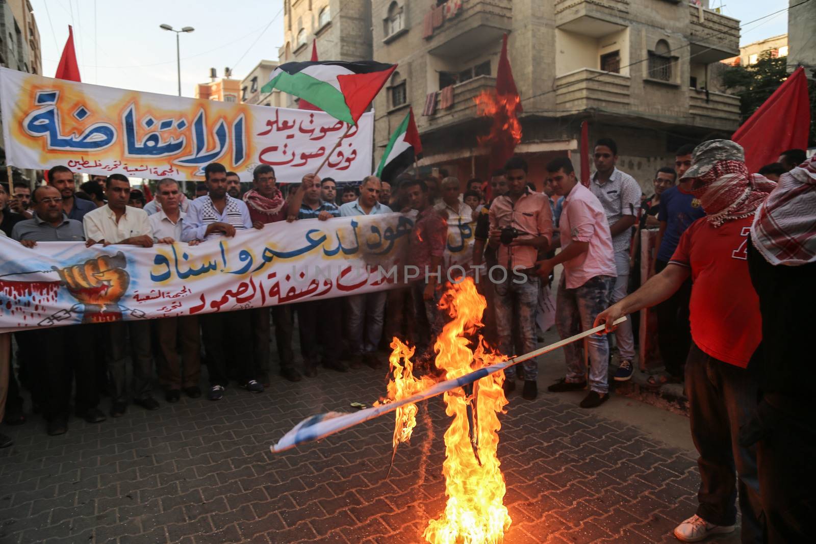 GAZA, Gaza City: A masked member of the Popular Front for the Liberation of Palestine burns a flag while protesting in Gaza on October 20, 2015. The group is rallying against what it perceives to be Israeli aggression in Jerusalem, the occupied West Bank and Gaza region over the past month, during which an upsurge of violence, including stabbing and gun attacks, has led to the deaths of at least 37 Palestinians and seven Israelis.    